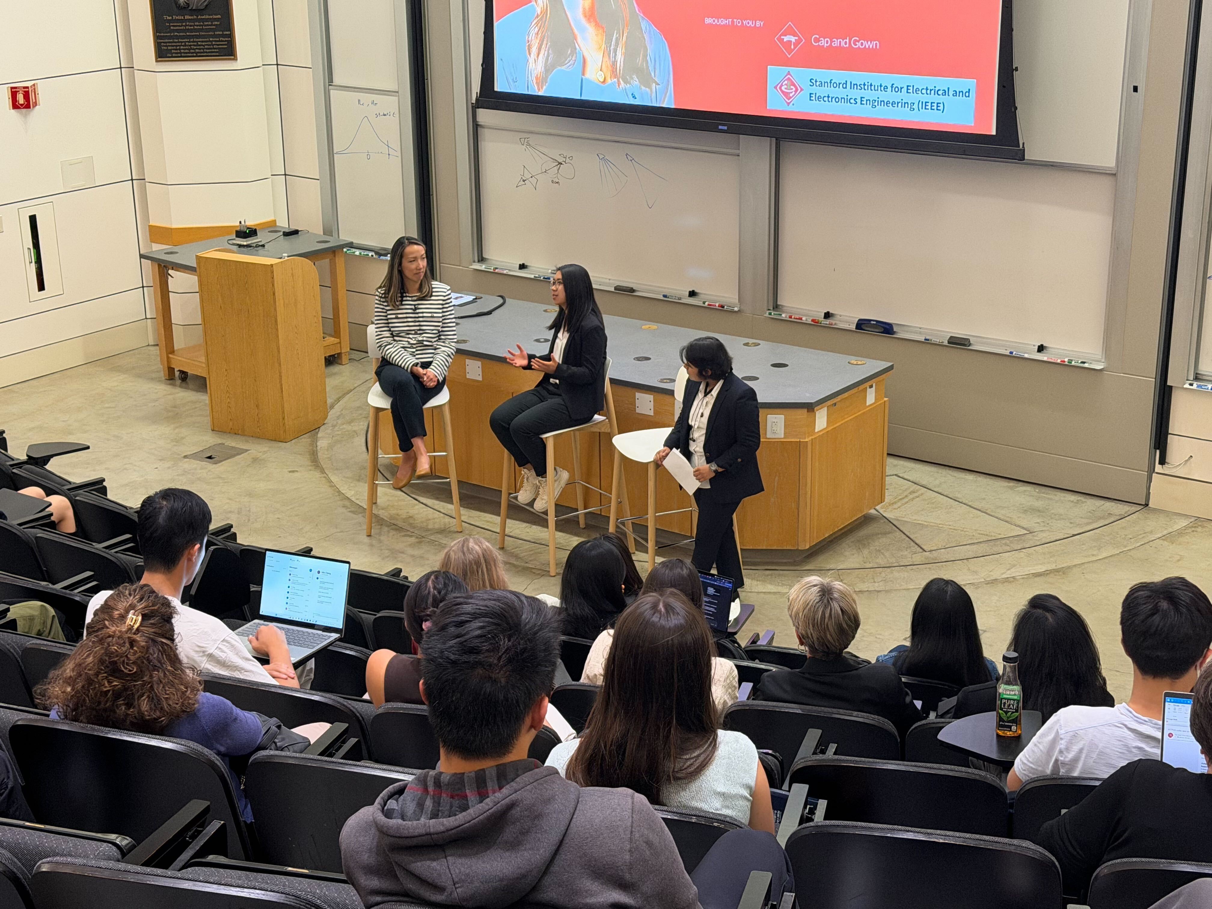 Clara Shih seated at the left of a Stanford fireside chat, facing students in a lecture hall