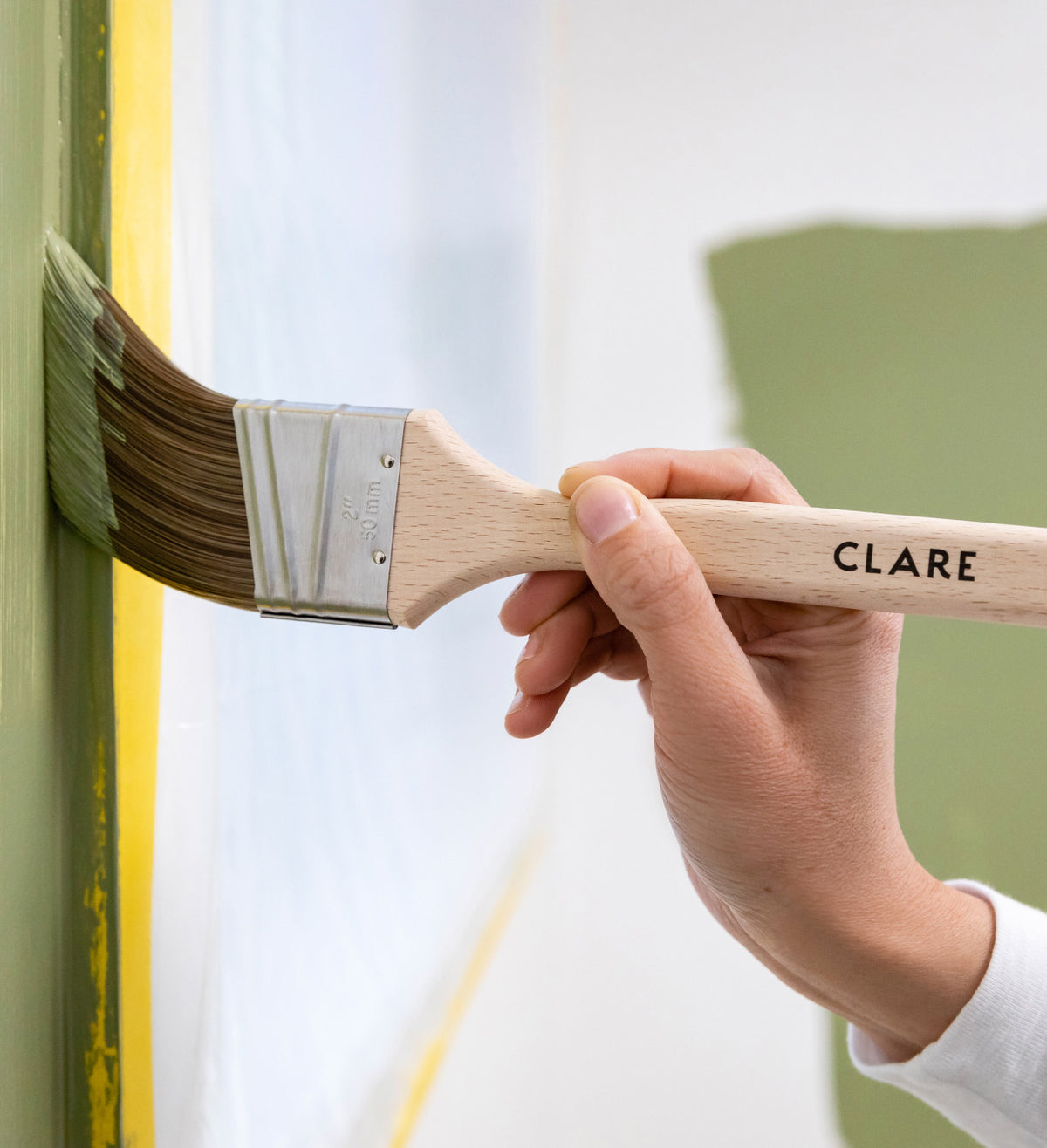 A Clare-branded brush applying green paint to a wall
