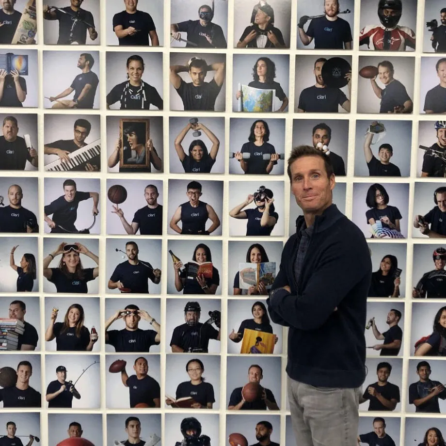 Clari co-founder Andy Byrne standing in front of employee portraits and their personal belongings
