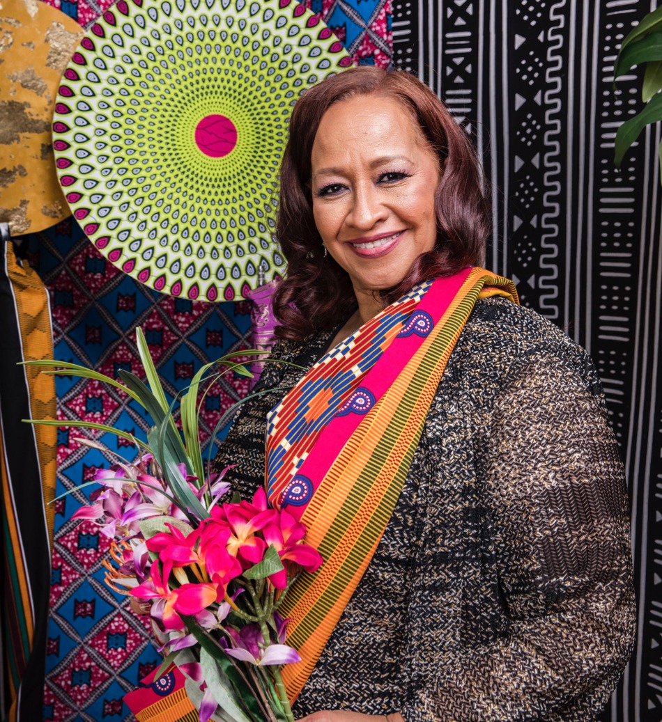 Priscilla Clarke standing before a colorful textile display