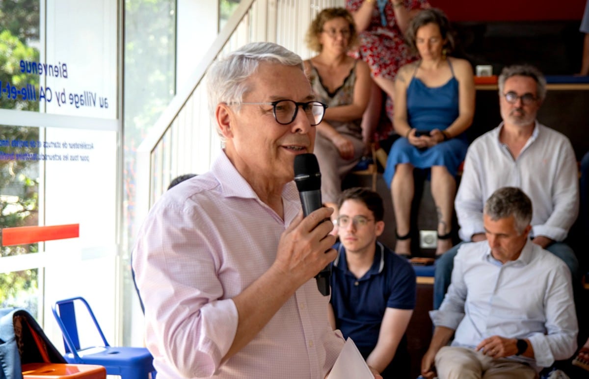 Claude Guillemot speaking into a microphone with an audience seated nearby at Village by CA