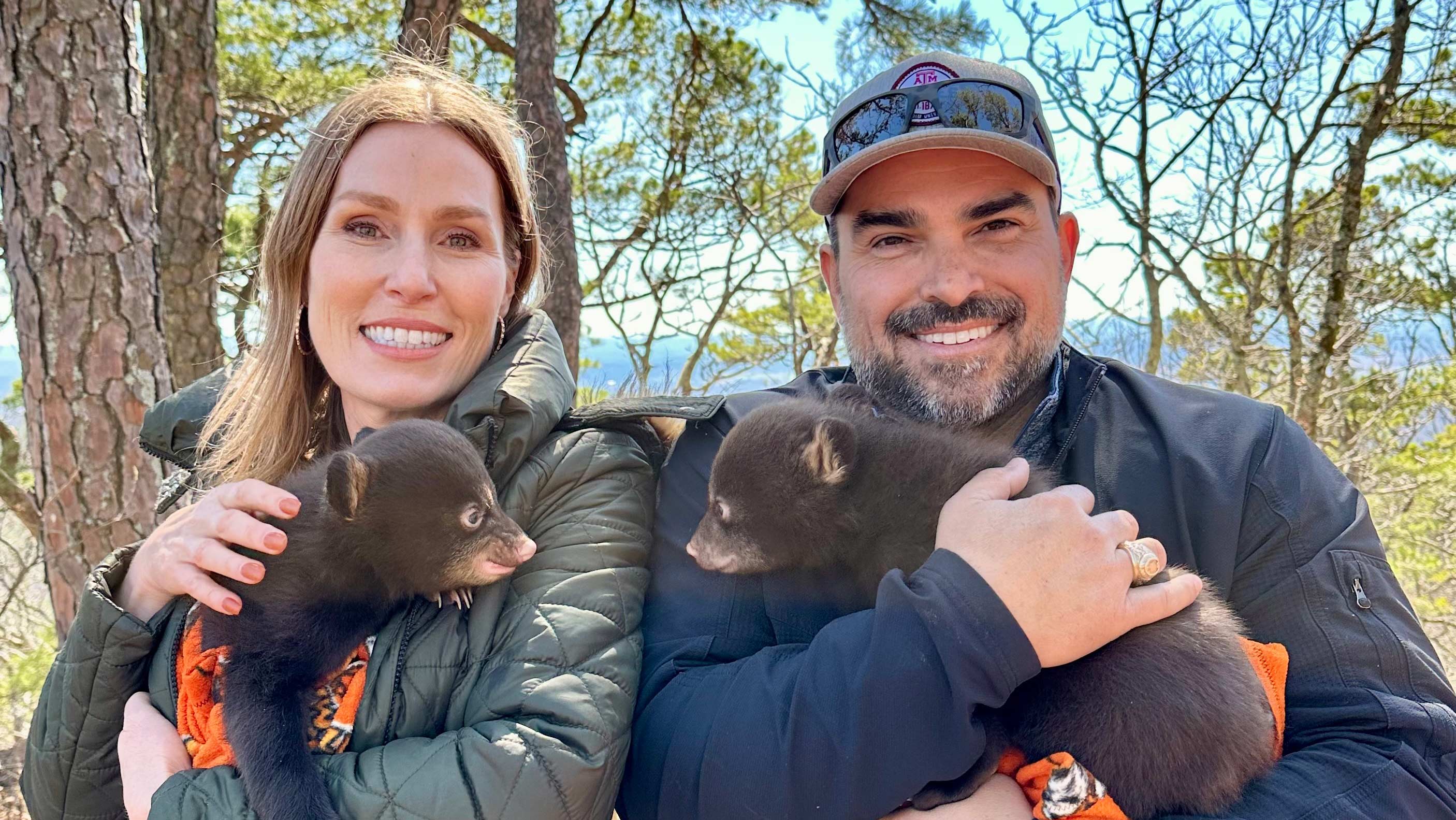 Leanne and Clay Gaspar outdoors, each holding a black bear cub during a conservation research visit