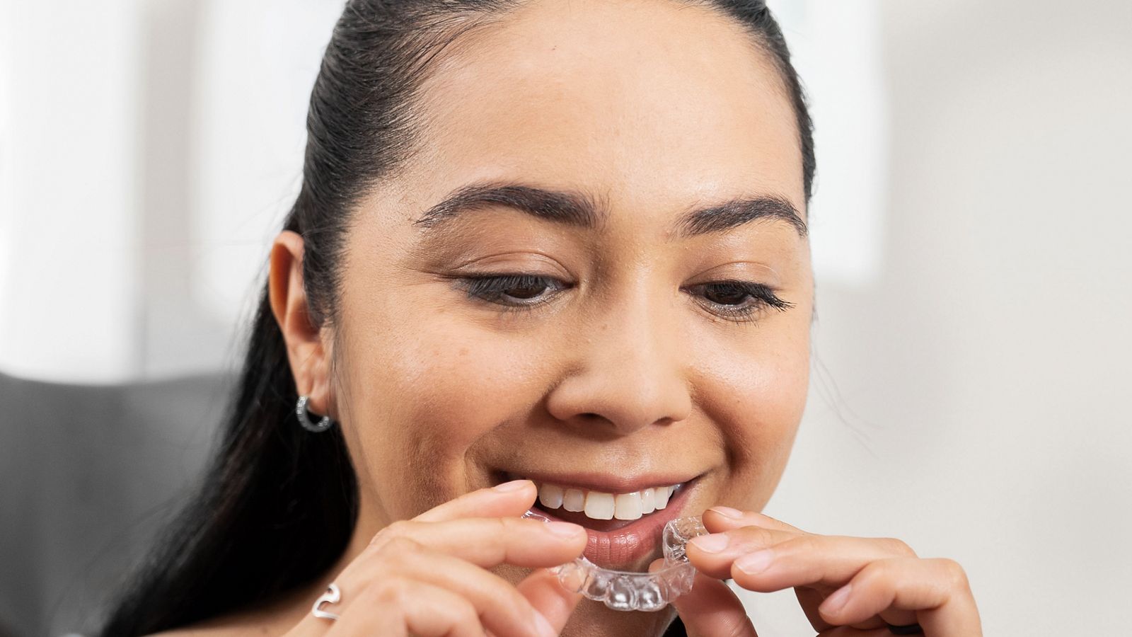 A patient holding a transparent aligner beside her teeth in a ClearCorrect promotional photograph