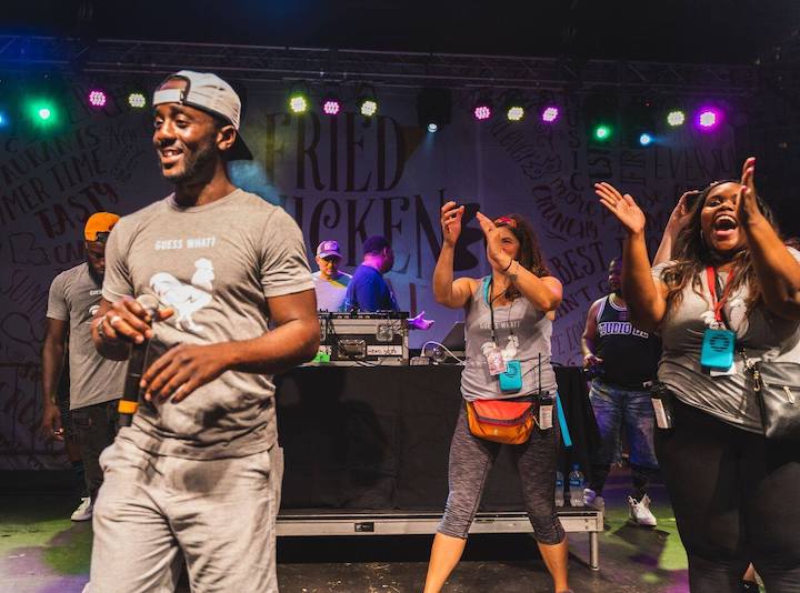 Cleveland Spears III holding a microphone on the Fried Chicken Festival stage, with smiling festival participants behind him