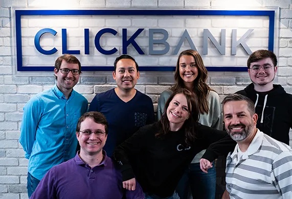Seven ClickBank colleagues gathered beneath the company’s office sign