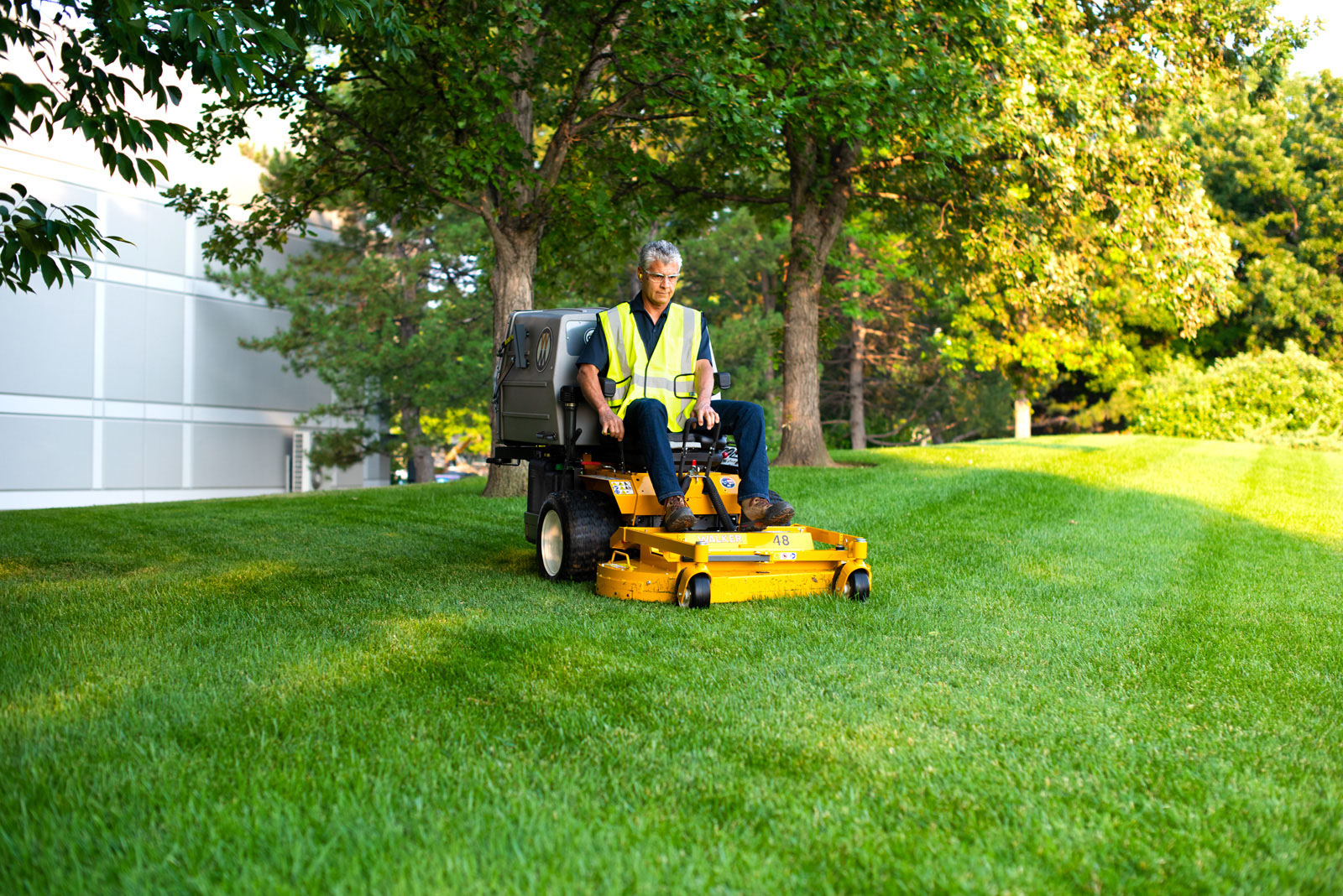 A worker driving a yellow Walker mower across a lawn