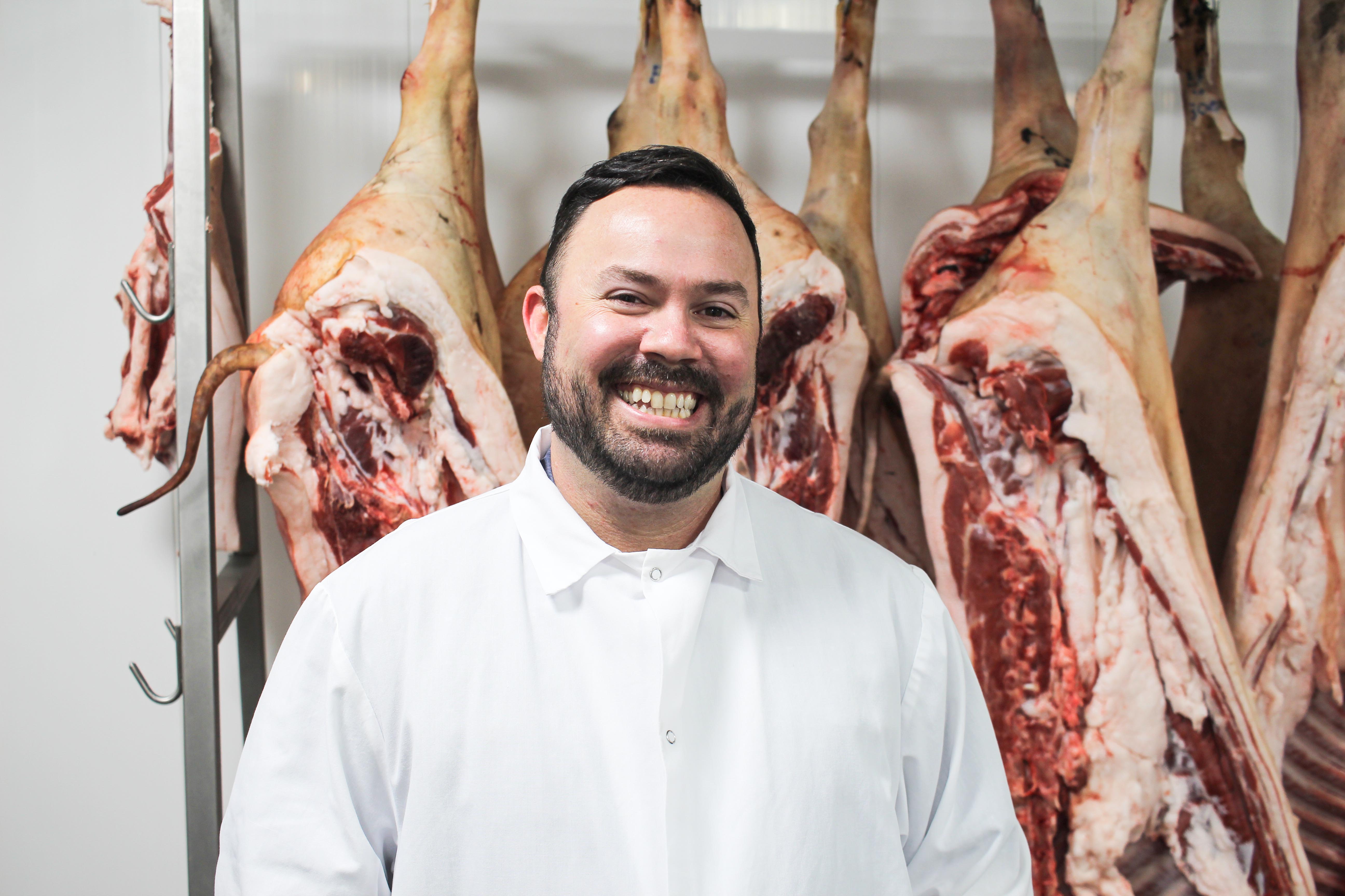 Cliff Pollard smiling in a white work coat inside Cream Co. Meats' processing facility
