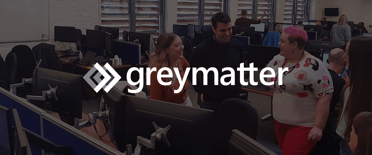 Grey Matter colleagues talking among desks and computer monitors in their office