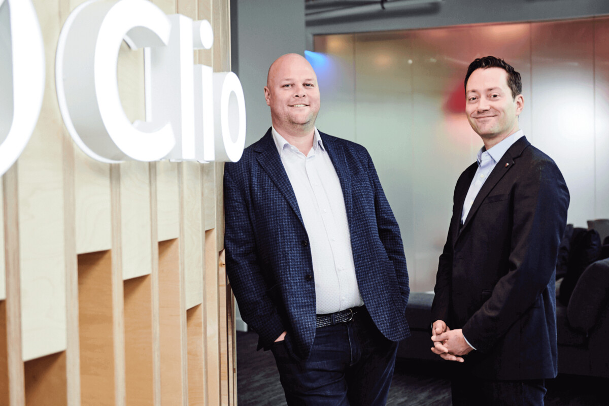 Clio co-founders Jack Newton and Rian Gauvreau standing beside a Clio sign in an office
