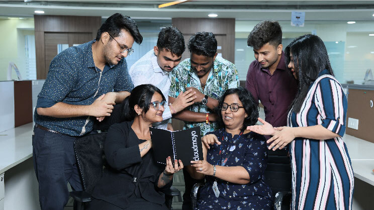 CloudMoyo team members gathered around an open company notebook in an office