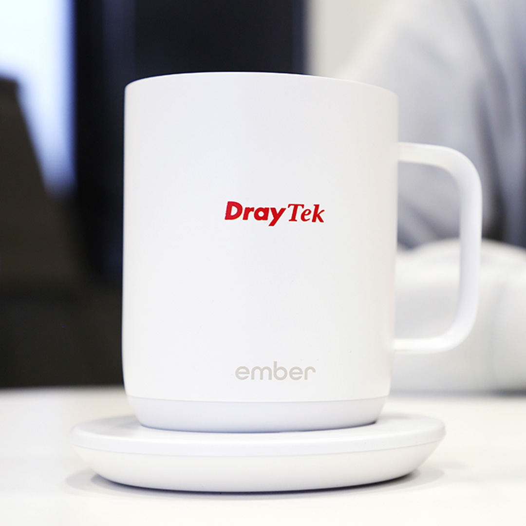 White Ember temperature-controlled mug with a red DrayTek logo, resting on its charging base