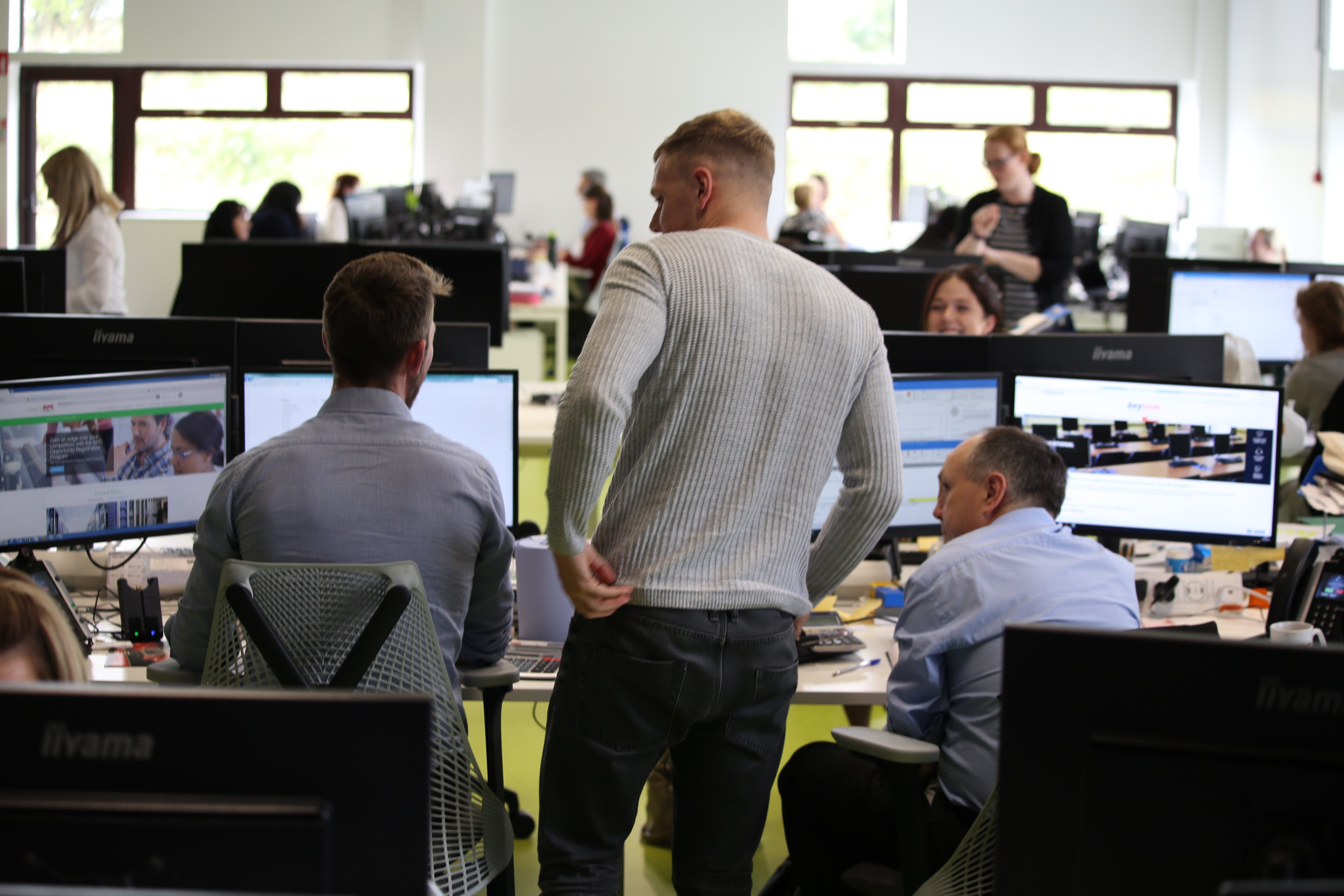 CMS colleagues discussing work among rows of monitors in an open-plan office
