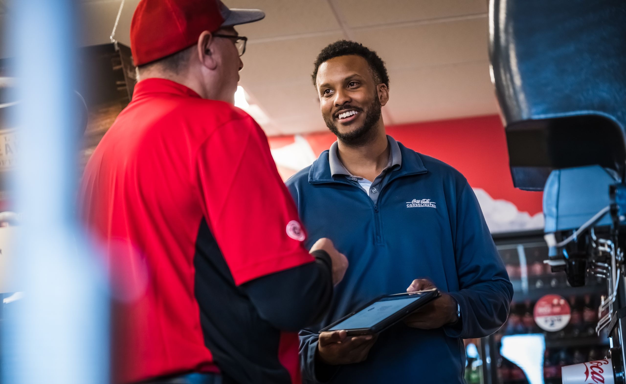 Coca-Cola Consolidated merchandiser speaking with a customer beside beverage equipment