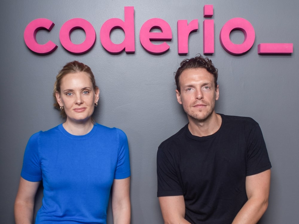 Coderio cofounders Eugenia Kessler and Joaquin Quintas seated beneath the company’s pink lettering