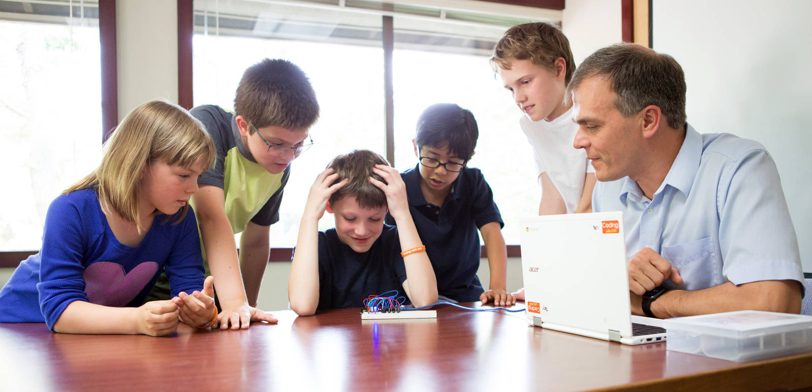 Children and an instructor gathered around a laptop and an electronics project