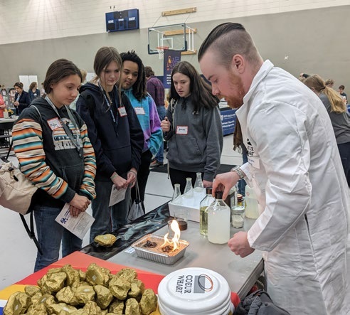 Participants watch a hands-on science demonstration in a photograph accompanying Wharf’s education outreach