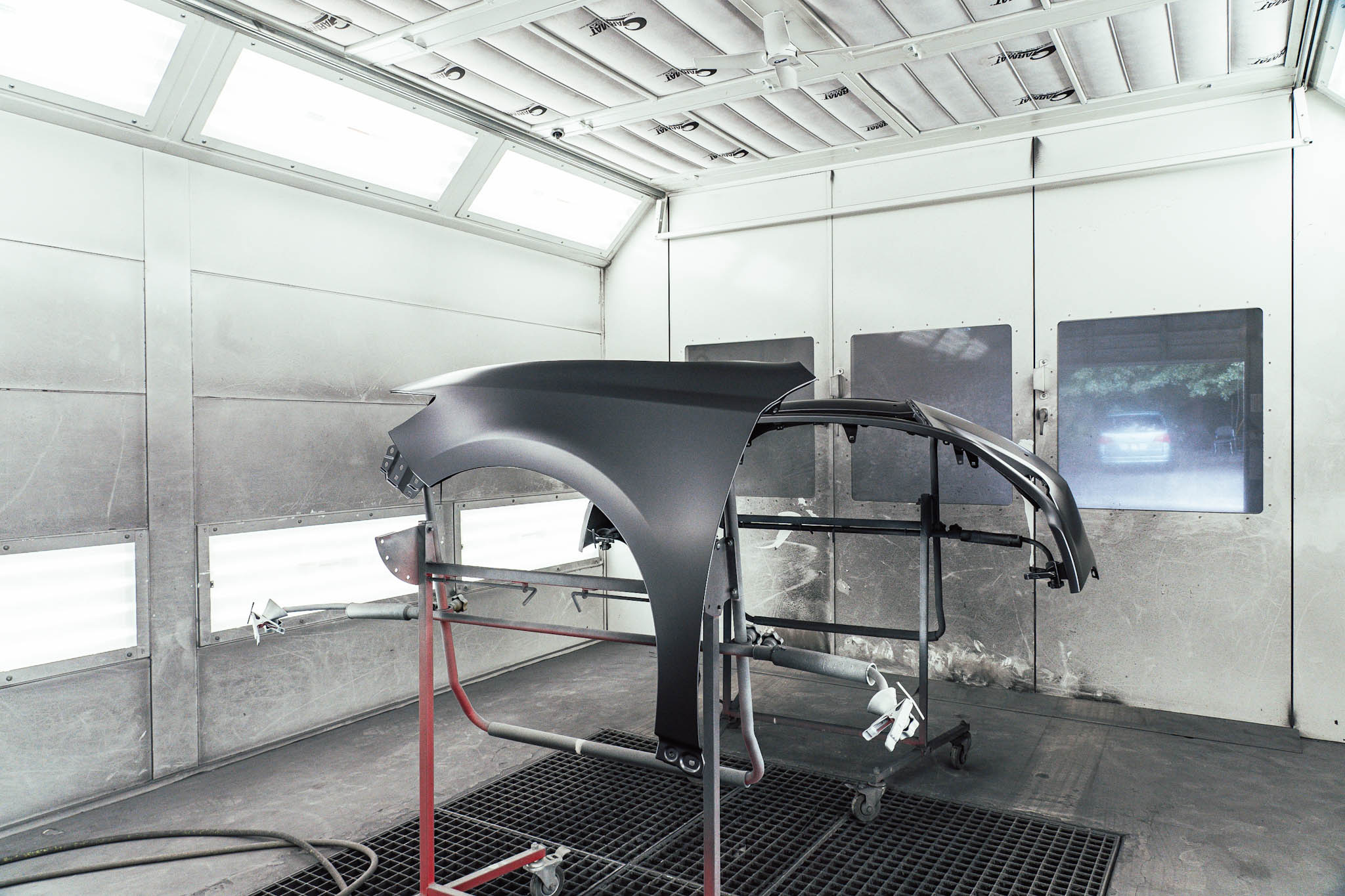 Detached vehicle panels on stands inside a paint booth, an image used by Coggin Collision