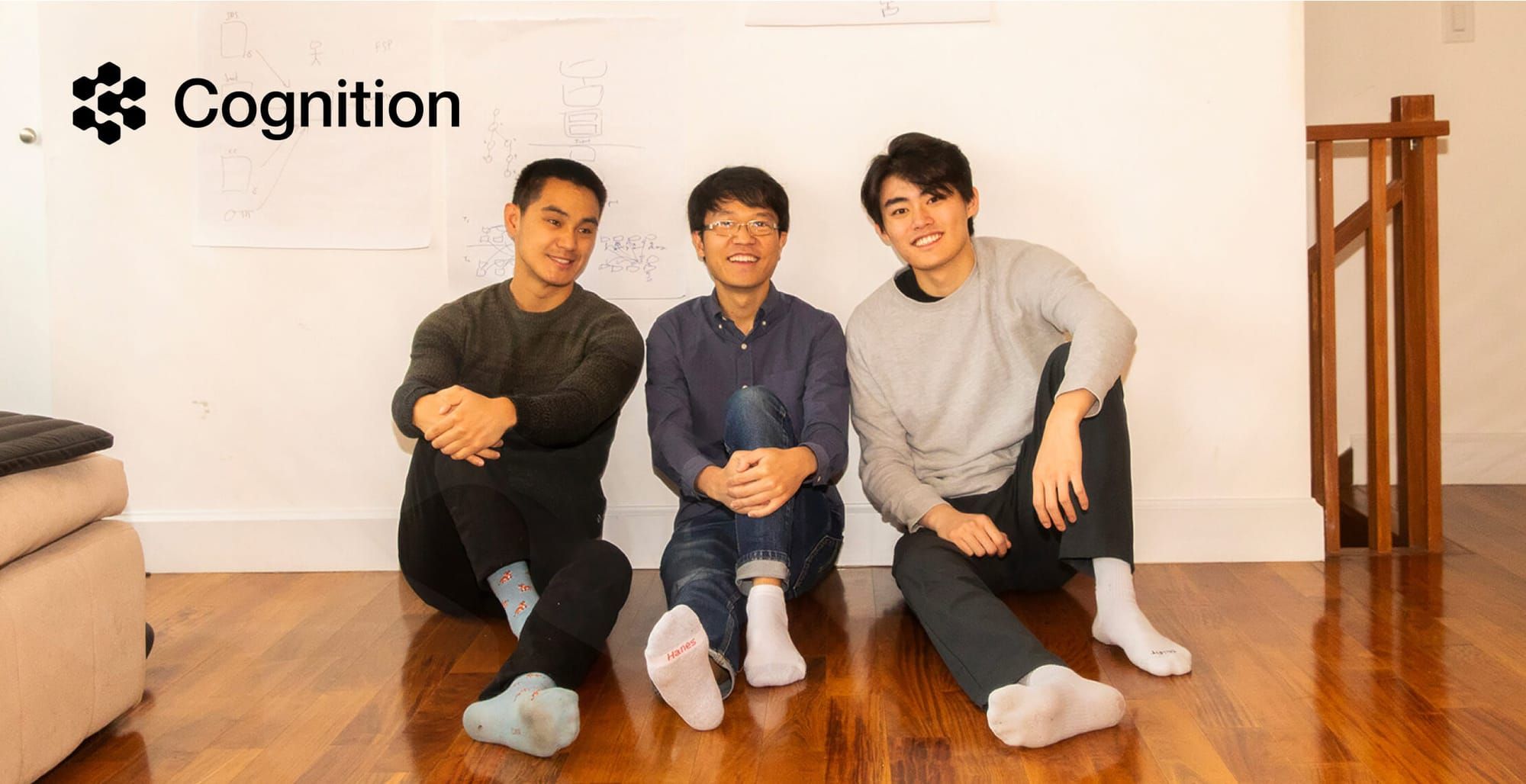 Three early Cognition founders seated on a wooden floor in front of diagrams