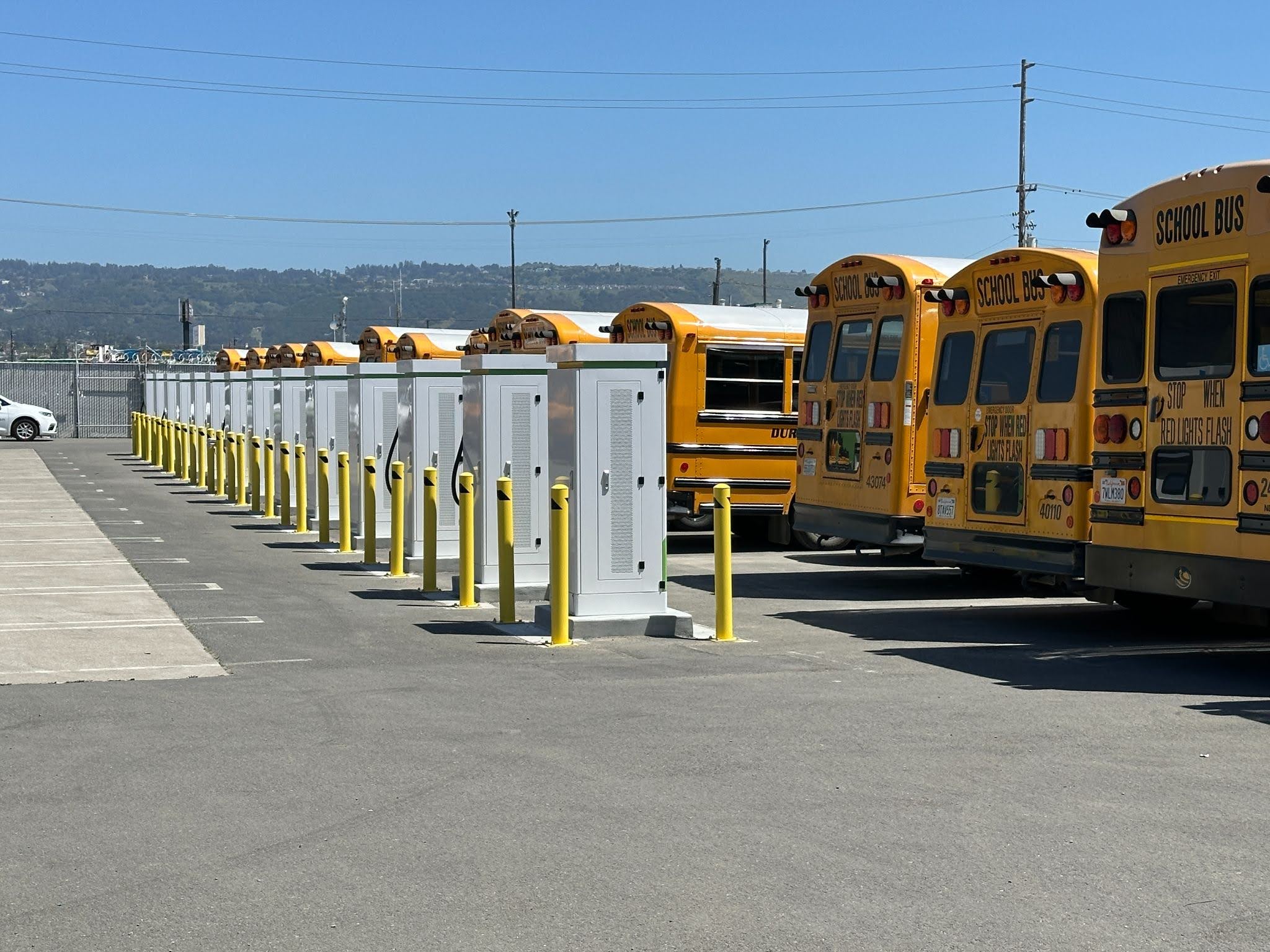 Rows of charging cabinets beside yellow school buses at an electrified bus yard
