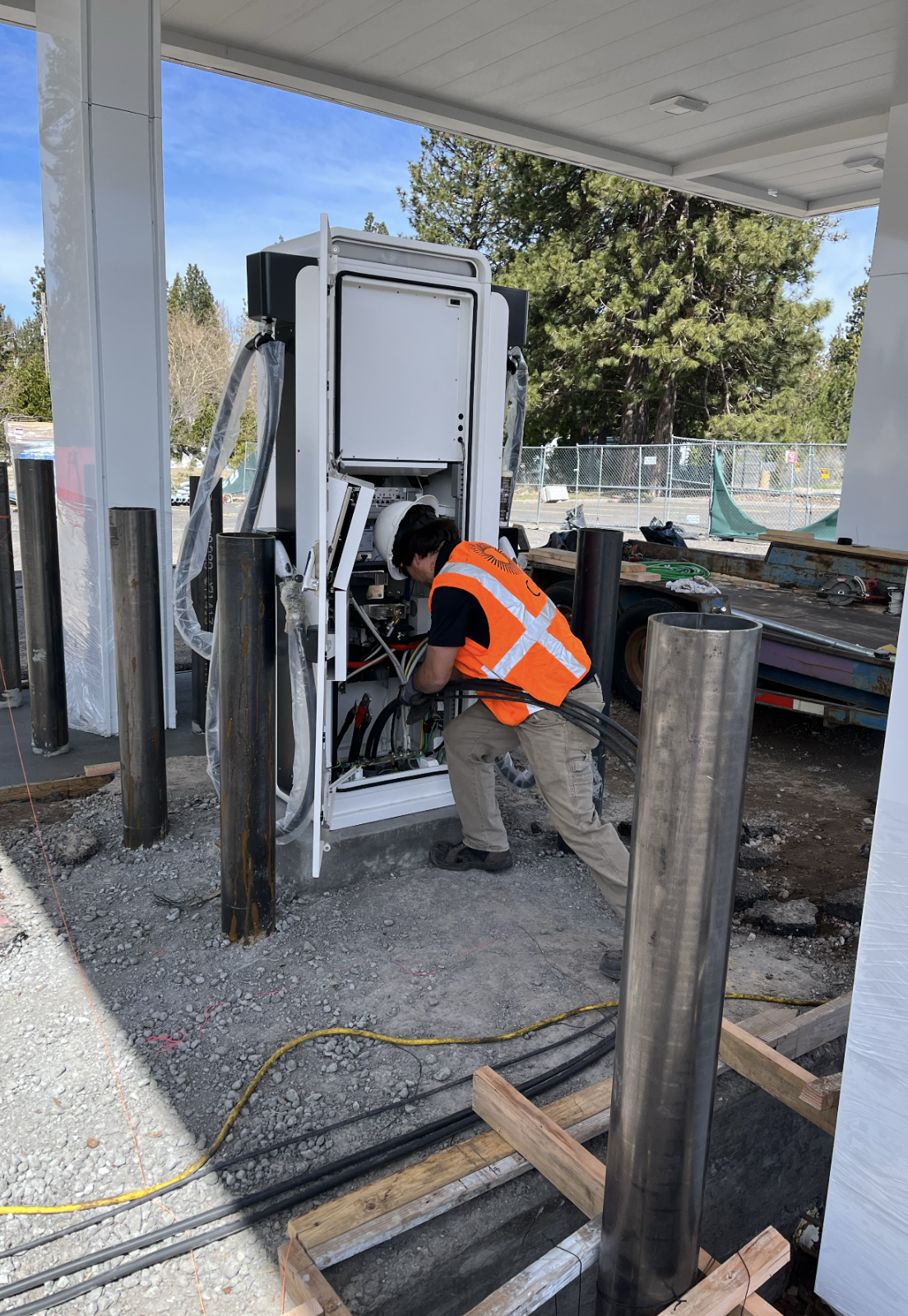 A COIL technician in an orange safety vest wiring a large fast-charging cabinet