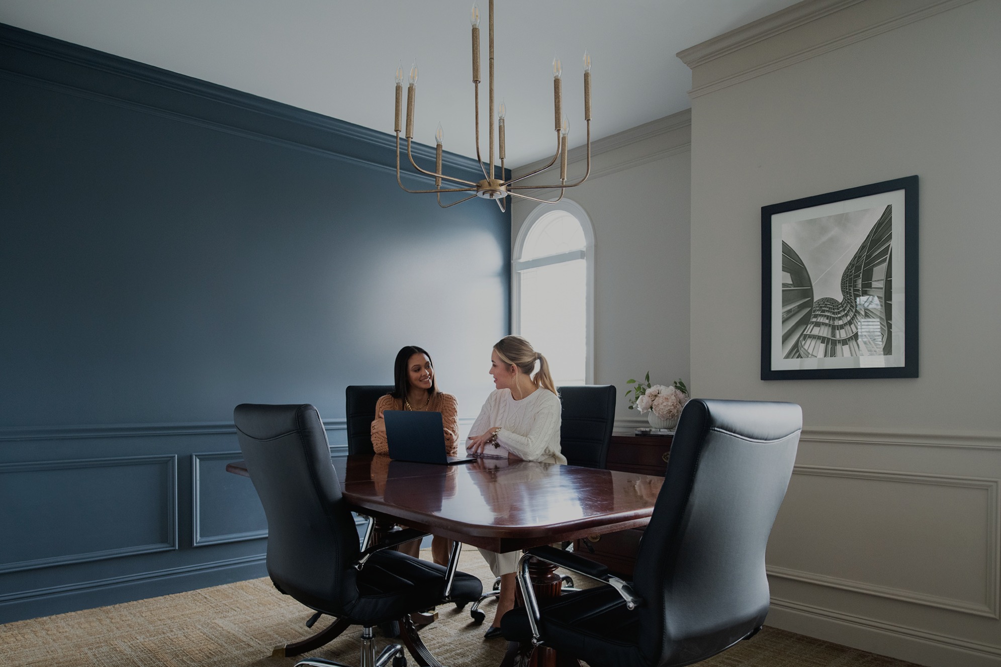 Two women talking across a laptop at a conference table in company marketing photography