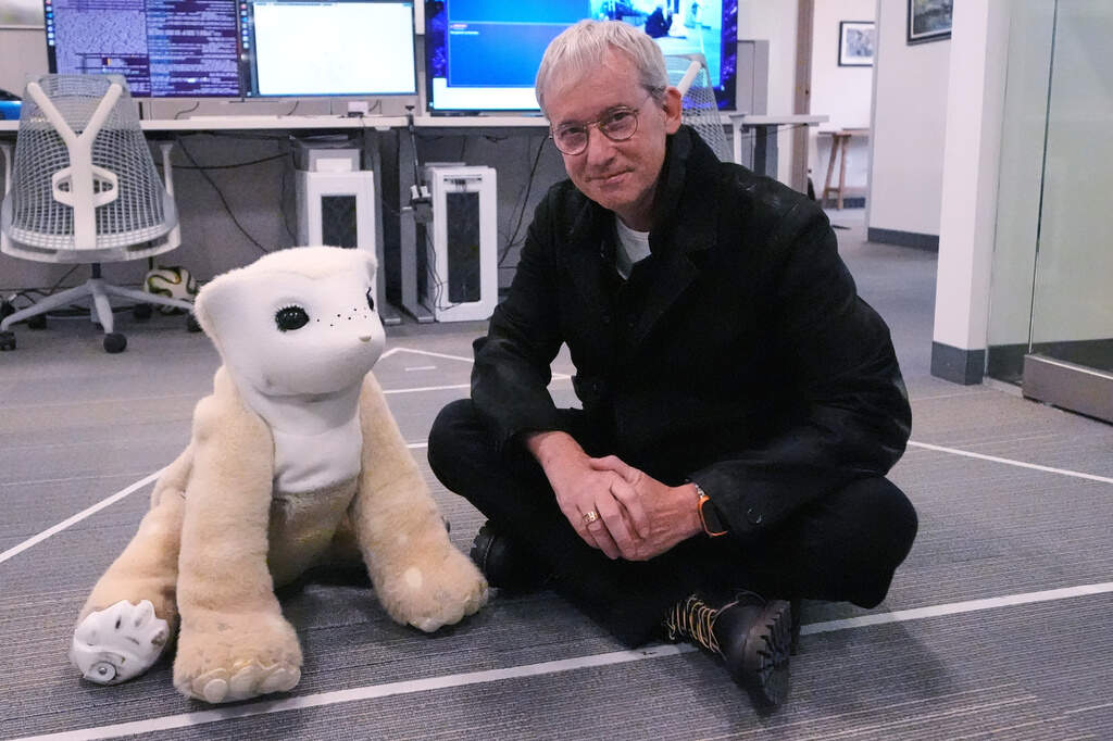 Colin Angle seated on the floor beside a Familiar robot prototype in the Woburn office