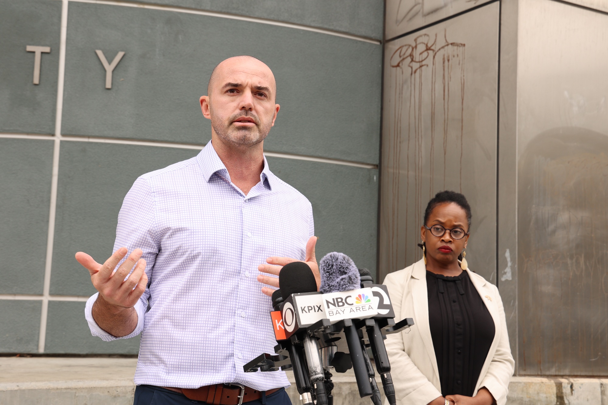 Colin Behring addressing reporters outside 415 20th Street with Oakland Councilmember Carroll Fife nearby