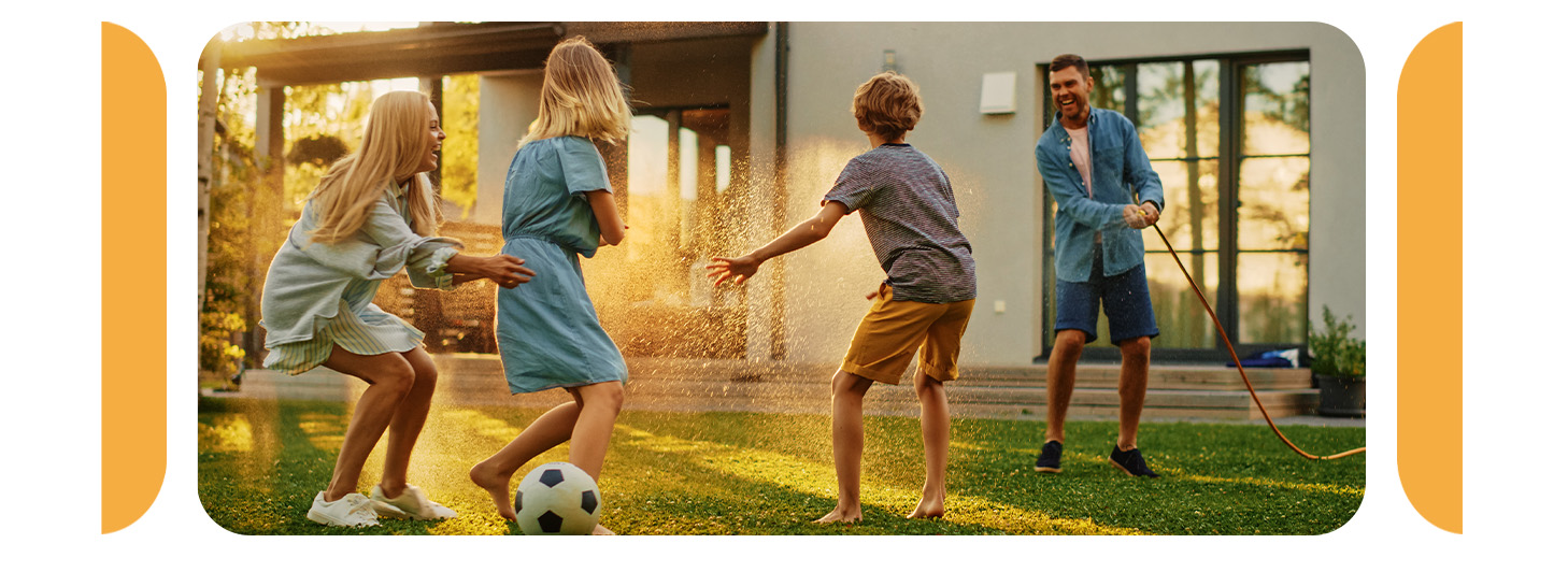 A family playing with a garden hose and soccer ball outside a home