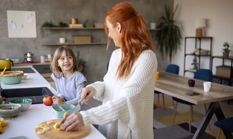 An adult and child prepare food together in a kitchen, in Jovie’s nanny-service photograph.