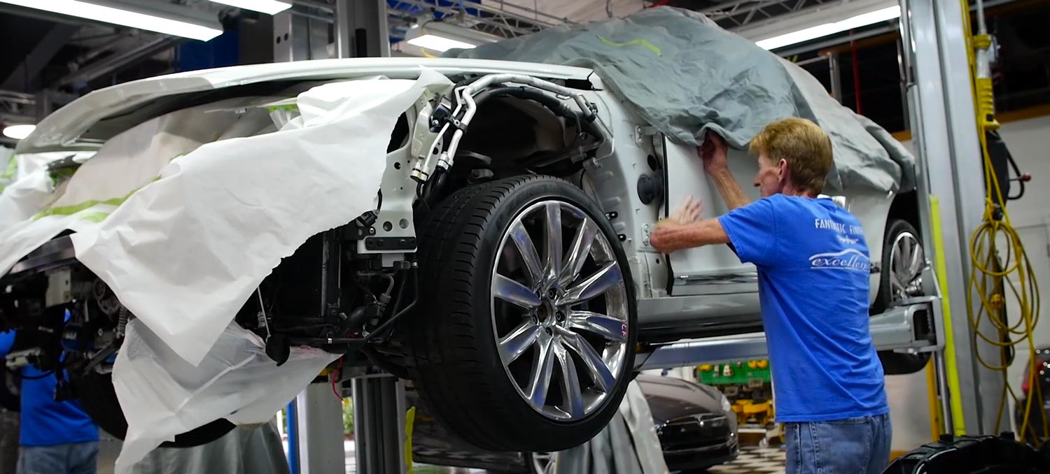 A collision-repair technician fitting a body panel to a vehicle inside a repair facility