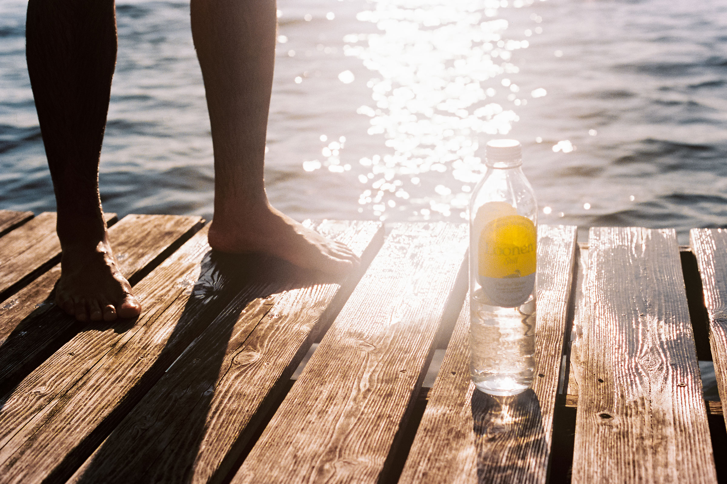 A bottle of Loonen water on a sunlit wooden dock beside a lake