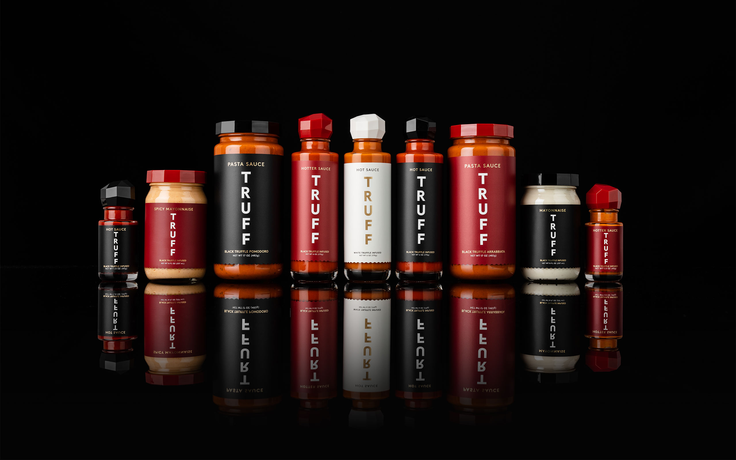 A lineup of TRUFF hot sauces, pasta sauces and mayonnaise on a reflective black surface