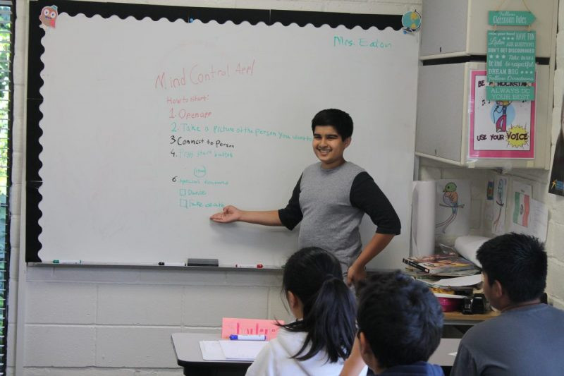 A Communication Academy student presenting beside a classroom whiteboard