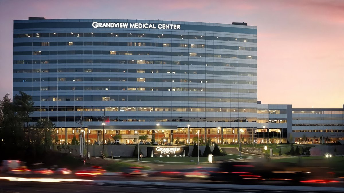 Grandview Medical Center’s glass hospital tower beside a busy road at dusk in Birmingham, Alabama