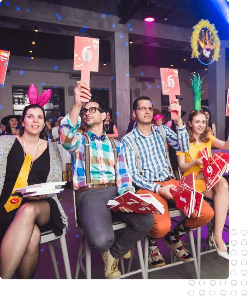 People at a Como team event holding score paddles and wearing colorful party accessories