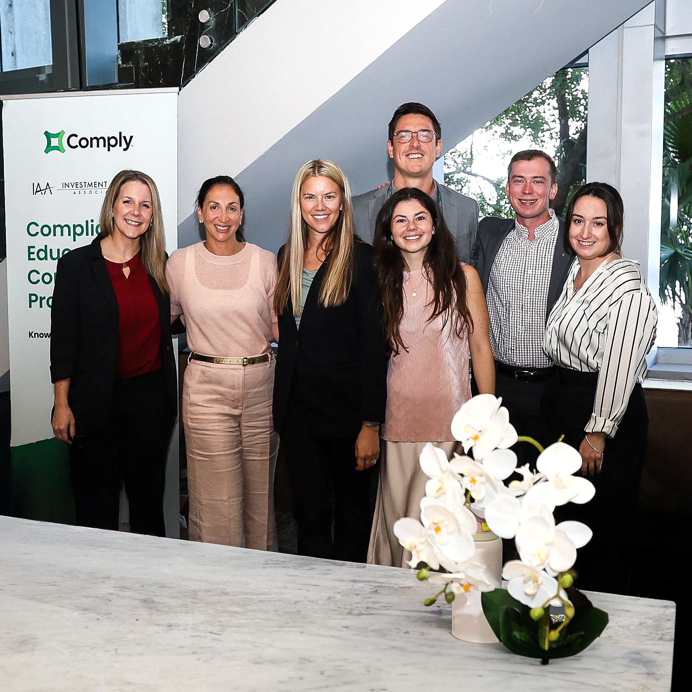COMPLY team members posing together beside a compliance education display