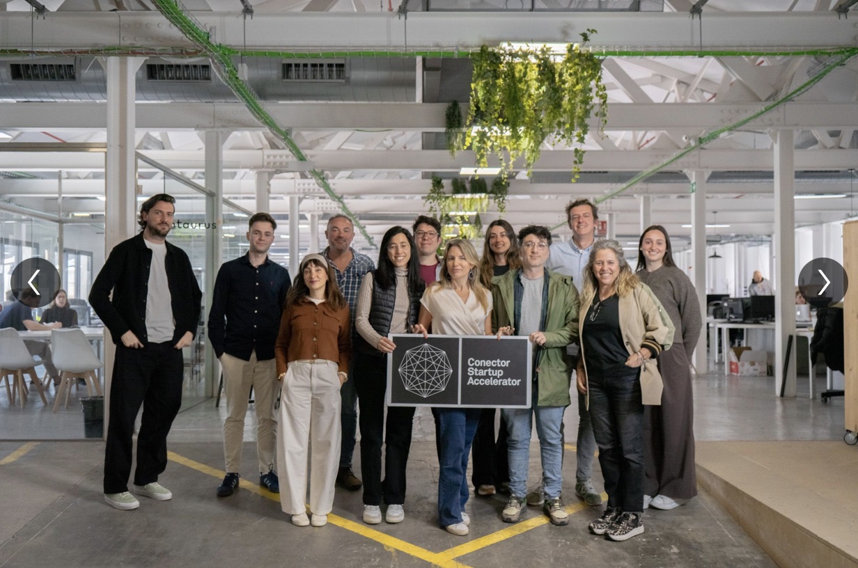 A Conector group standing together in a shared office and holding an accelerator sign