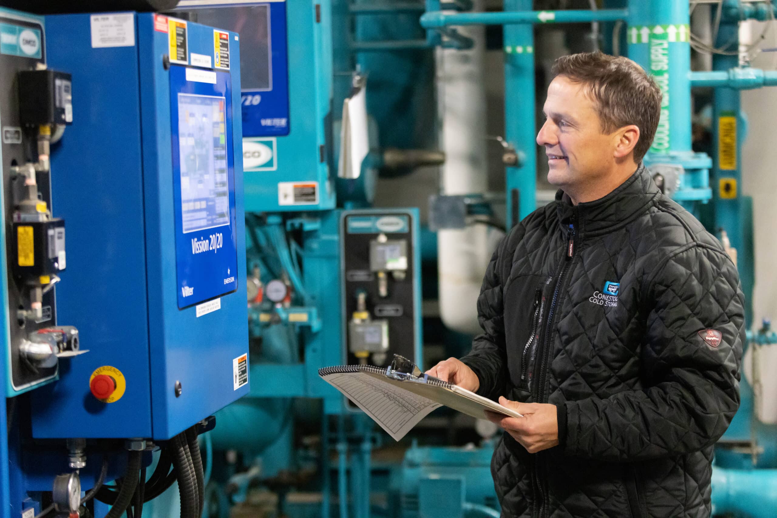 A Conestoga employee checks refrigeration equipment beside a control screen