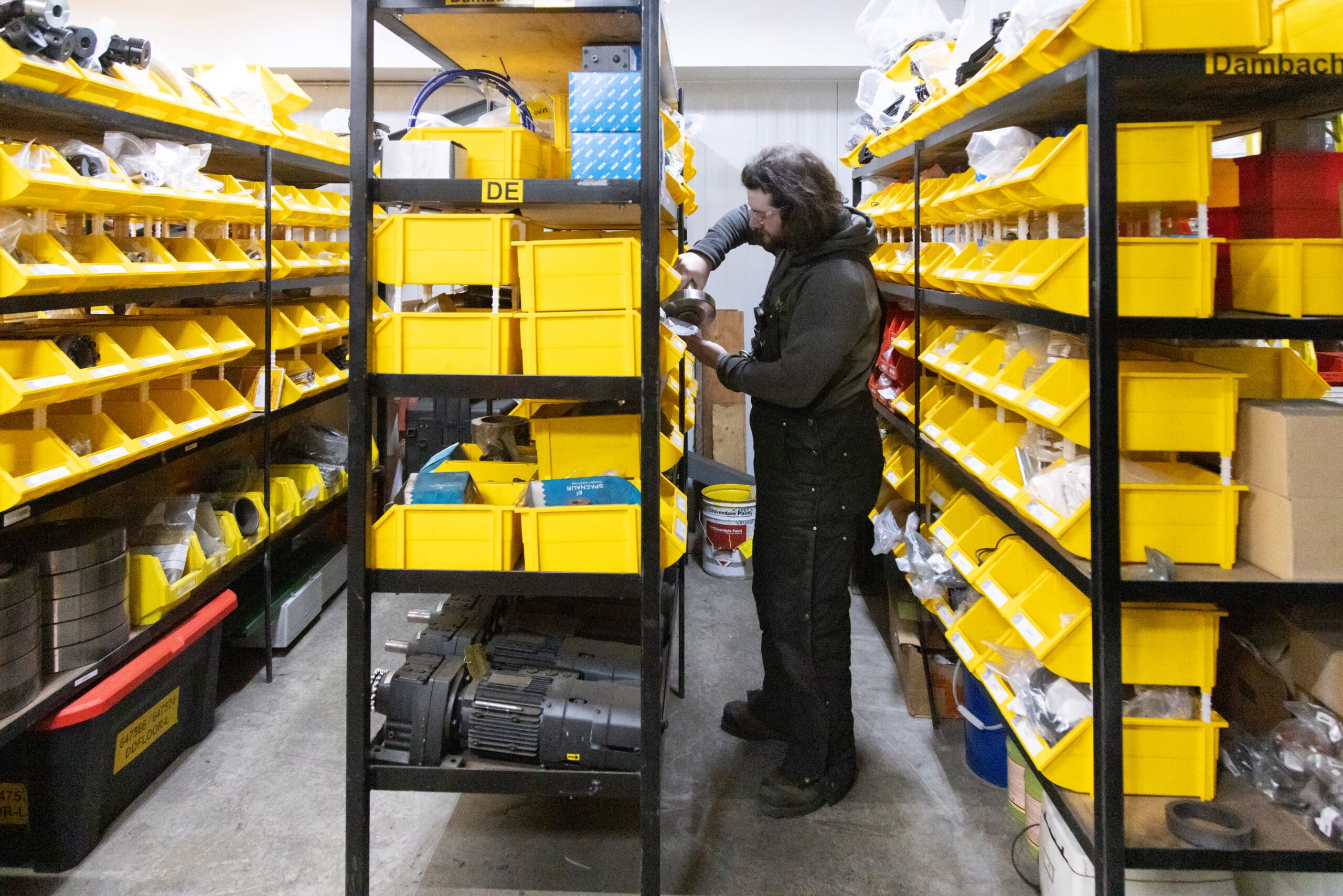 A Conestoga worker selects parts from shelves of yellow storage bins