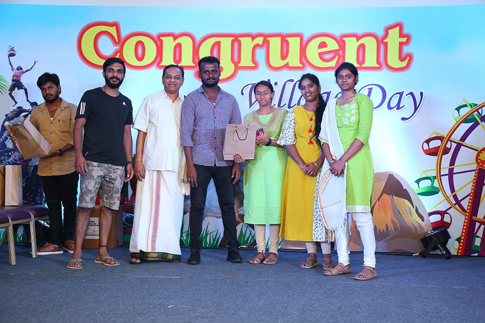 Congruent colleagues on a stage beneath a Village Day celebration banner