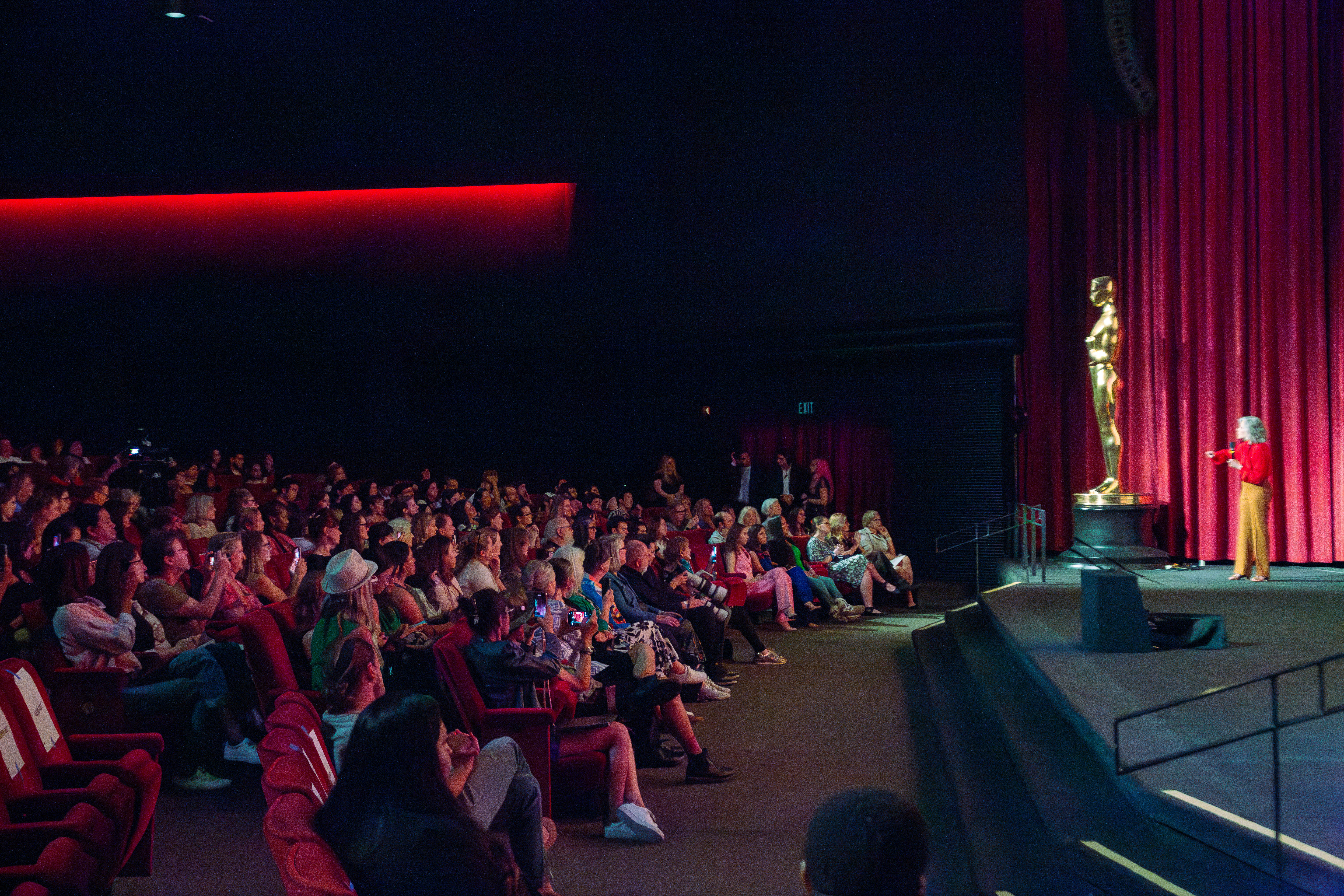 An audience watches a speaker beside an Oscar statue at Hollywood Climate Summit 2024