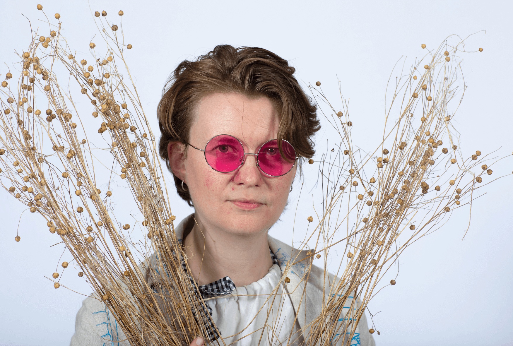 Fantasy Fibre Mill co-founder Rosie Bristow holding flax stems, wearing round pink glasses