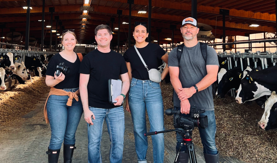 Four C.O.nxt team members with cameras and production gear inside a dairy barn