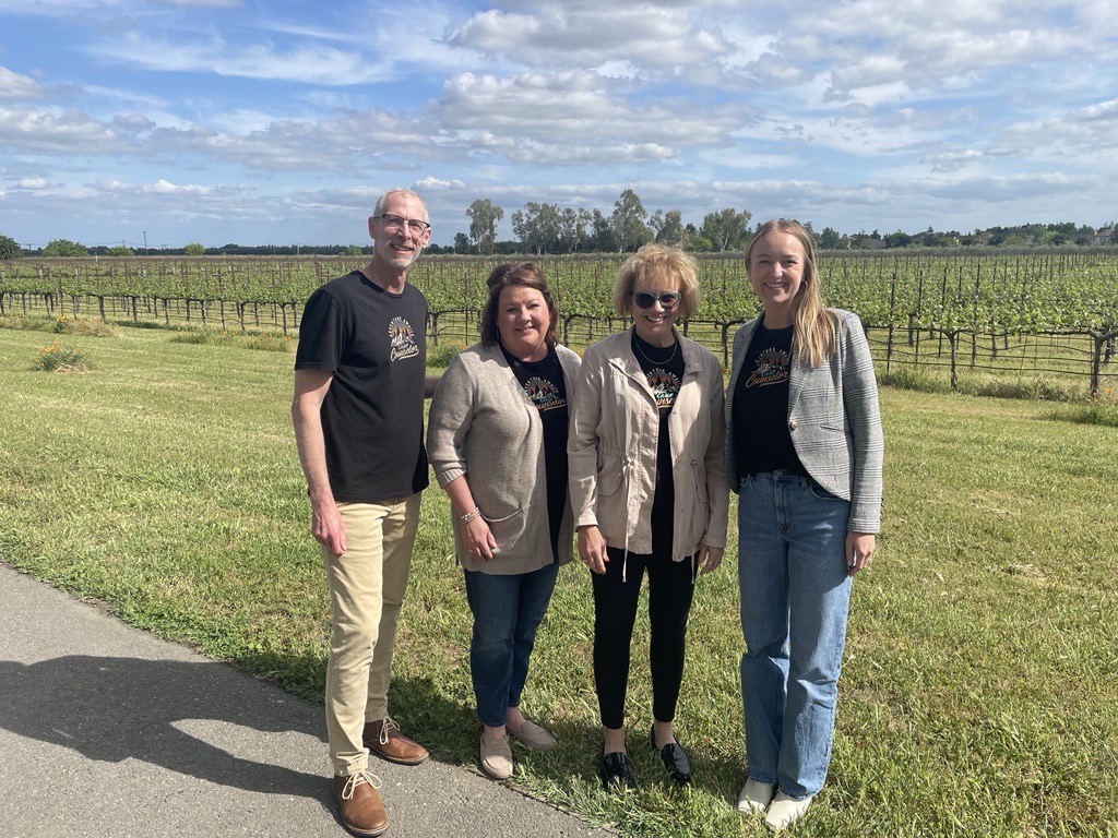 Four C.O.nxt colleagues standing beside a vineyard under a broad blue sky