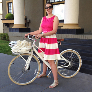 Corinne Winter standing beside a white bicycle, wearing a pink top and striped skirt