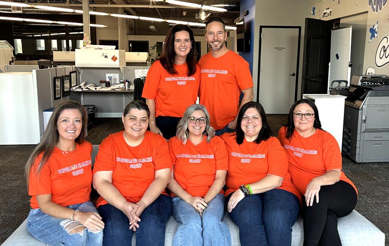 Seven Corporate Cleaning Group team members in orange shirts, pictured in an office