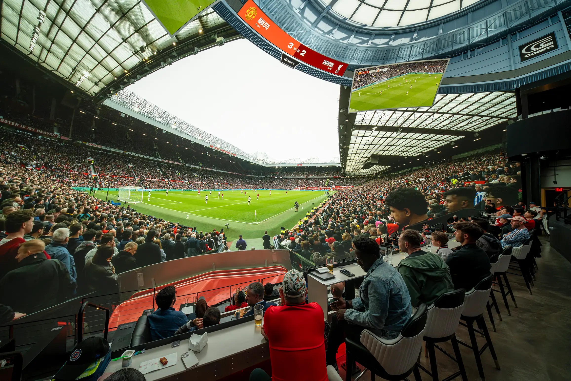Fans seated at tables inside Cosm with a Premier League stadium image surrounding them