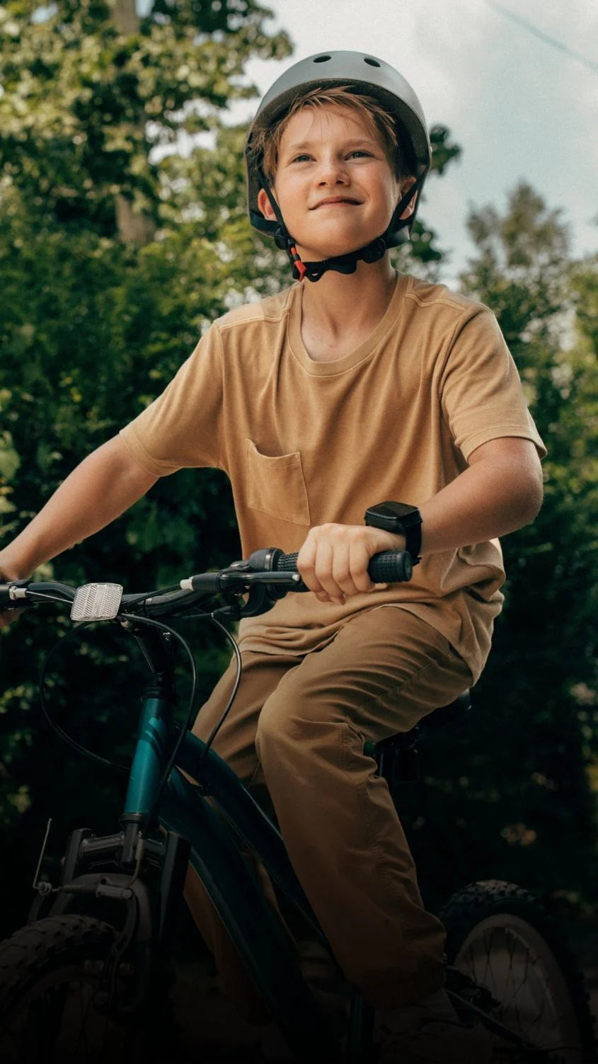 A boy in a helmet rides a bike outdoors wearing a Cosmo JrTrack watch on his wrist