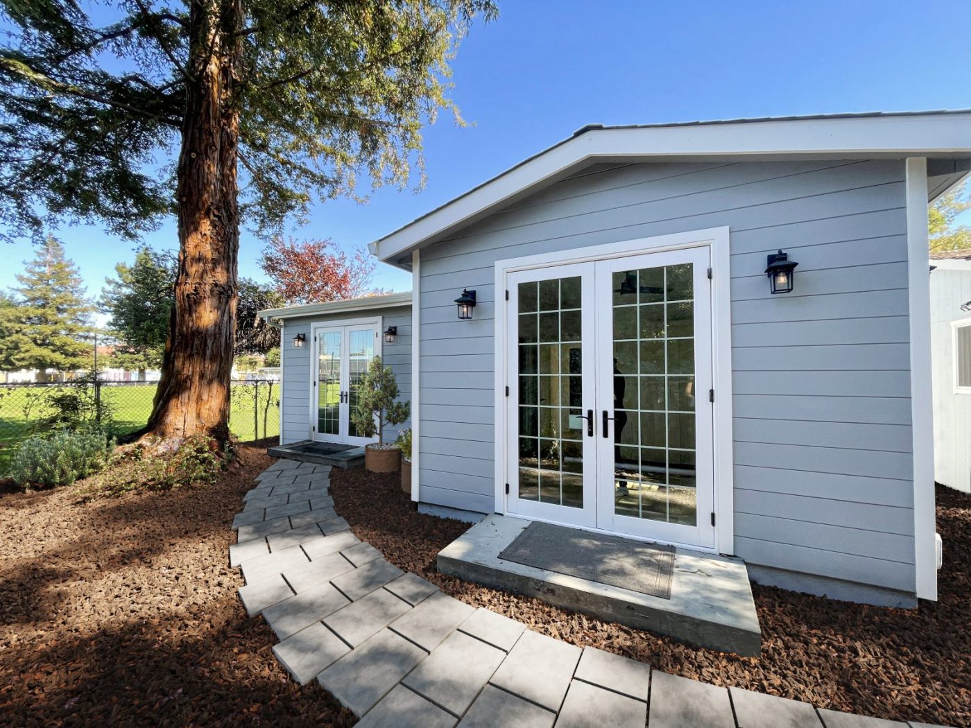 A completed Cottage accessory dwelling unit with pale siding and French doors beside a garden path