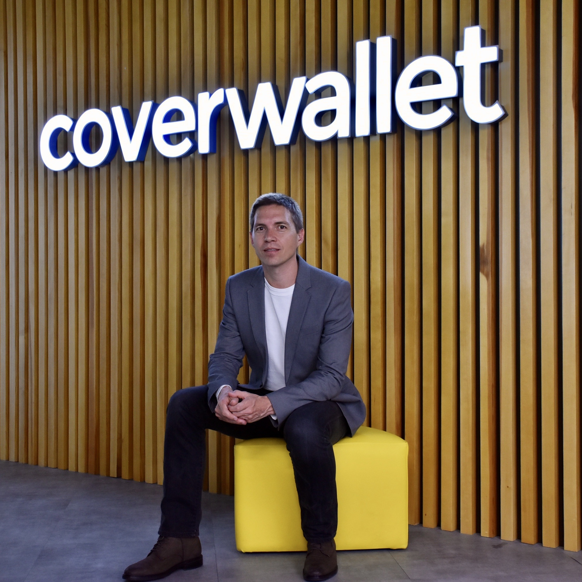CoverWallet co-founder Iñaki Berenguer seated on a yellow bench in front of the company’s office sign